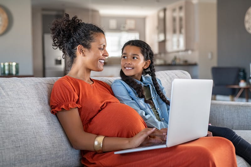 Pregnant woman working from home in maternity leave as daughter looks on
