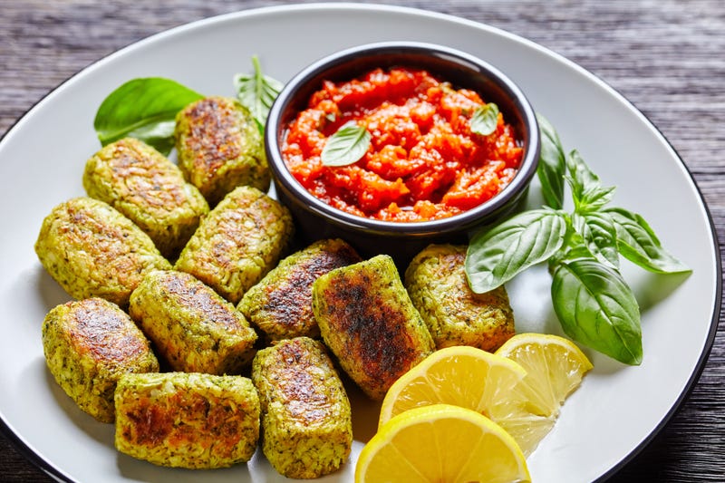 baked broccoli tots on a white plate with marinara sauce on a wooden table with ingredients on a cutting board