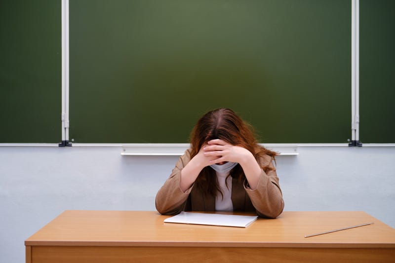 Upset teacher at desk in front of chalkboard.