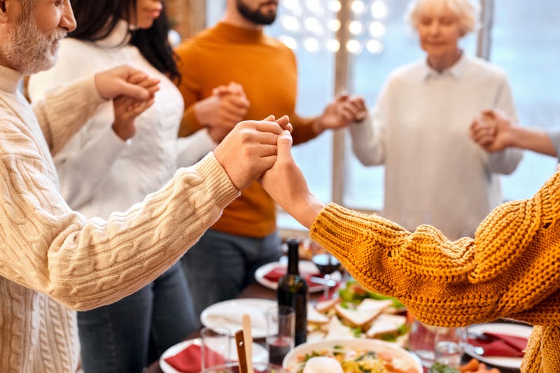 family holds hands during prayer before holiday dinner at home