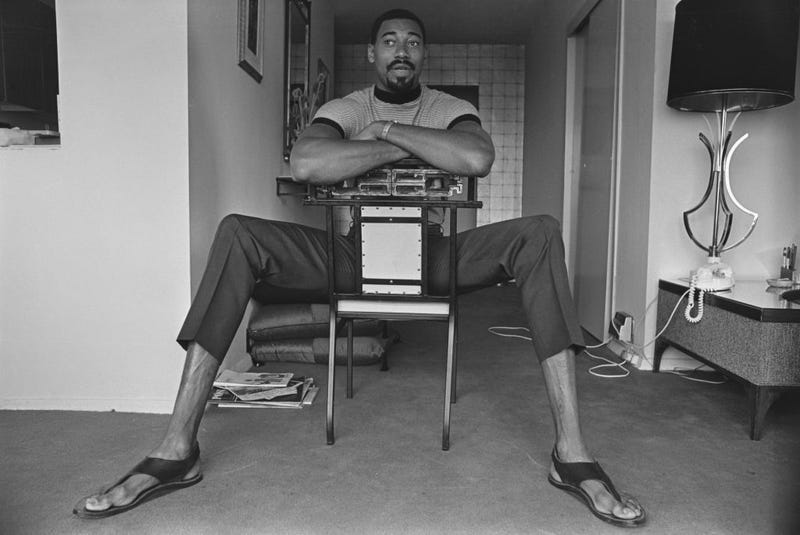 Wilt Chamberlain's height is on display even as he sits down in a chair.