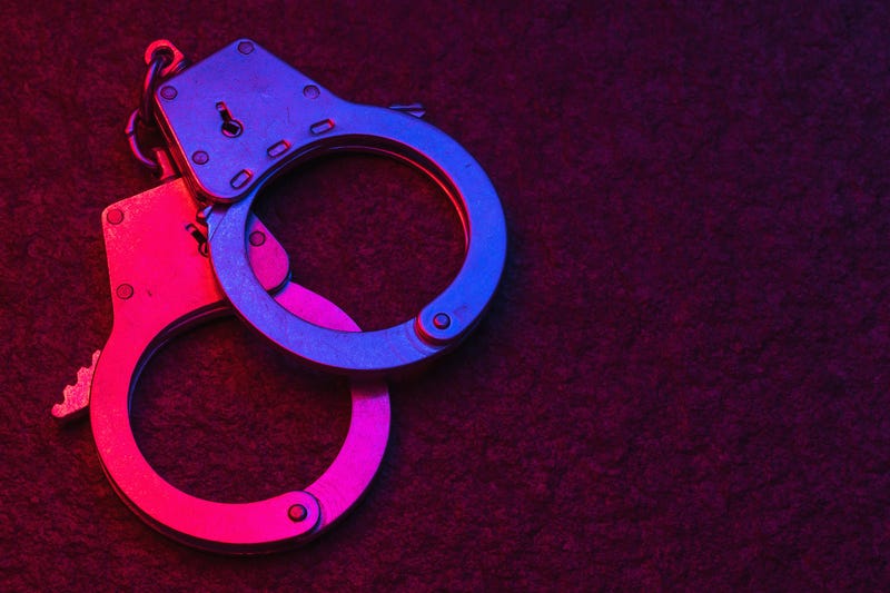 Handcuffs on dark background illuminated by flashing lights of police car with copy space