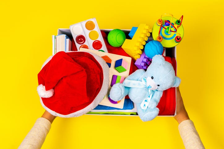 Hands holding donate box with clothes, books and toys on yellow background