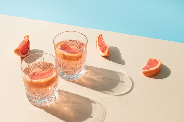 Two glasses of drink with slices of fresh grapefruit against bright beige and blue background