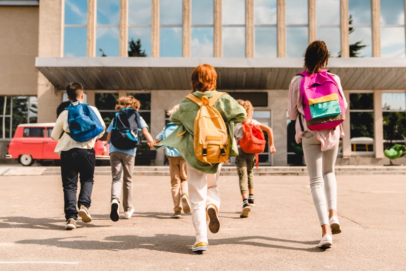 A group of children wearing backpacks walk up to a school