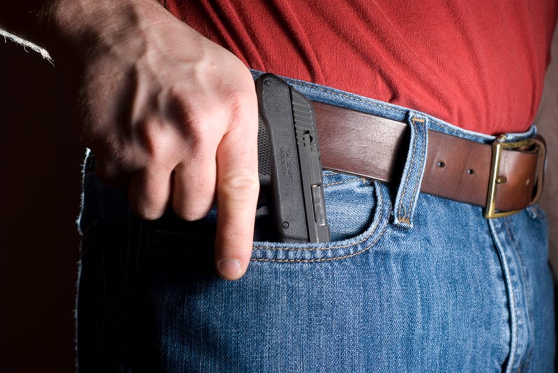 Man drawing a concealed pistol from the front pocket of a pair of jeans.