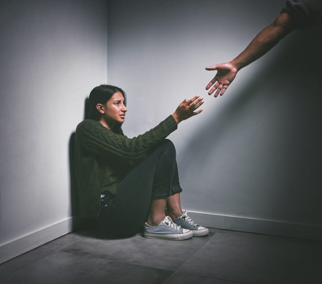 young woman sitting in the corner of a dark room with a hand reaching out to help her