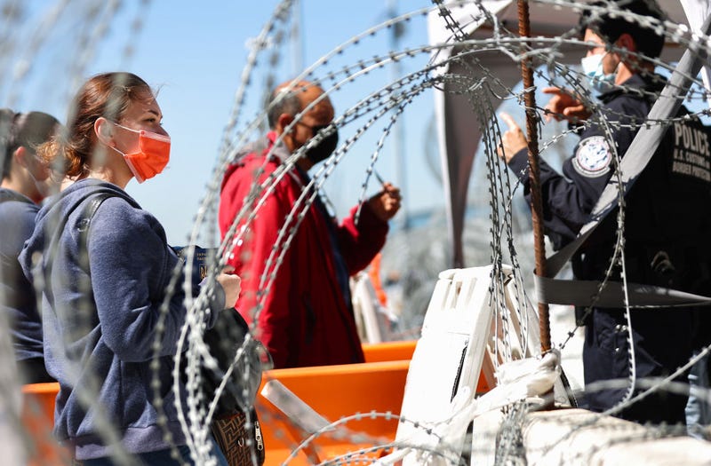 A person from Ukraine (L) holds their passport while waiting near a U.S. Customs and Border Protection officer before being allowed to cross the San Ysidro Port of Entry into the United States to seek asylum on March 22, 2022 in Tijuana, Mexico. U.S. authorities have recently been allowing Ukrainian refugees to enter the U.S. at the Southern border in Tijuana with permission to remain in the U.S. on humanitarian parole for one year.