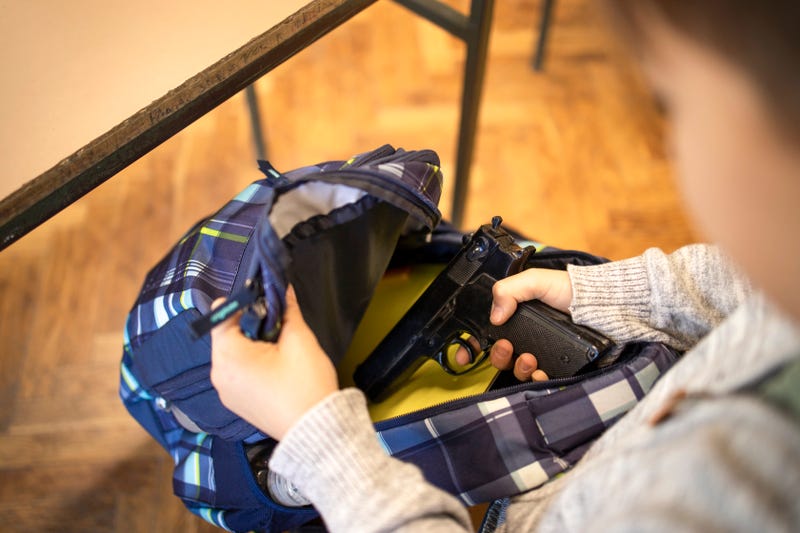 Child taking the pistol firearm out of school bag and preparing for mass shooting.