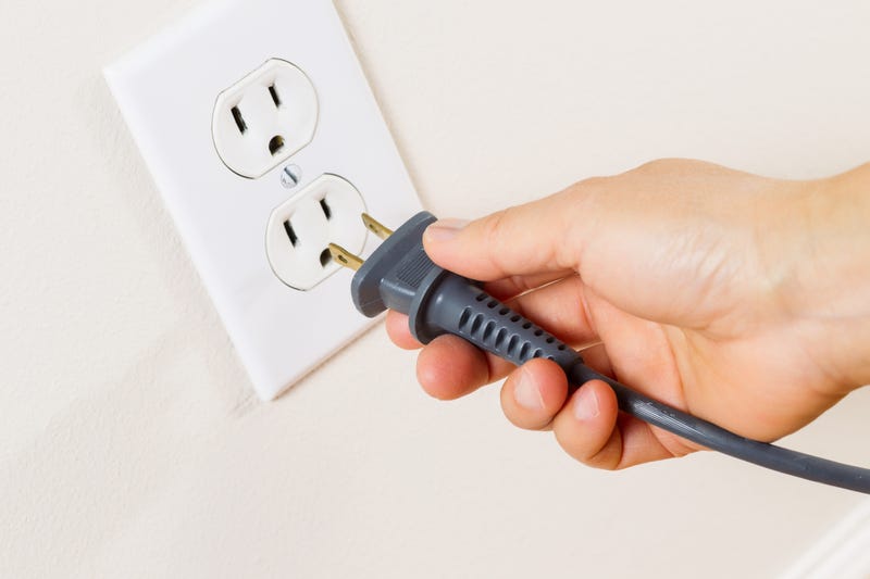 A hand unplugs a plug from an electrical outlet