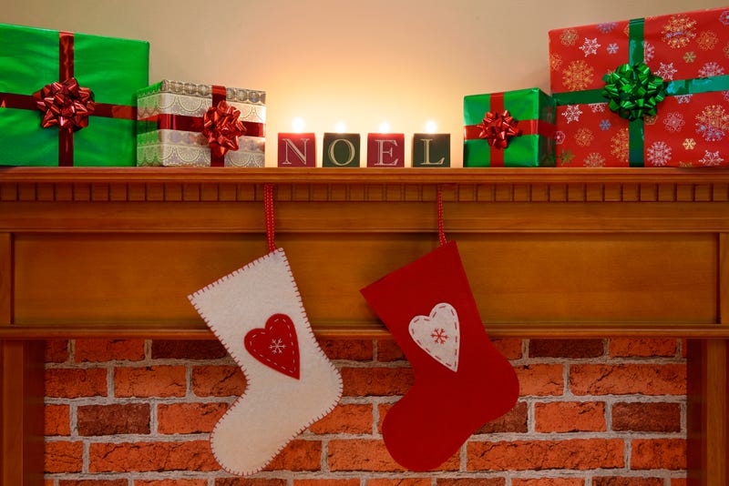 Wrapped presents sit on a mantle beside candles and other Christmas decroations