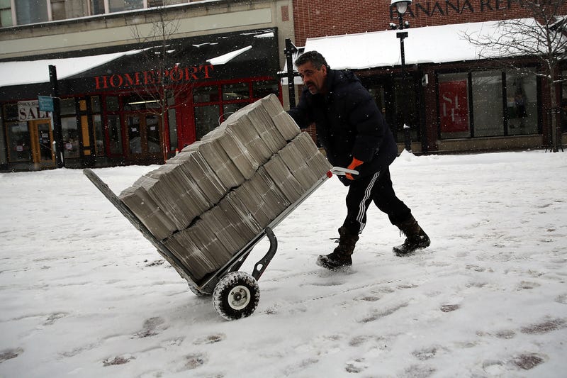 A newspaper deliverer wheels a trolley of newspapers through the snow