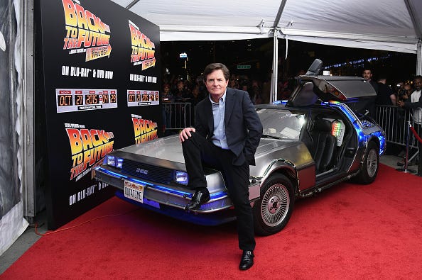 Michael J Fox sitting on a car at the Back to the Future red carpet