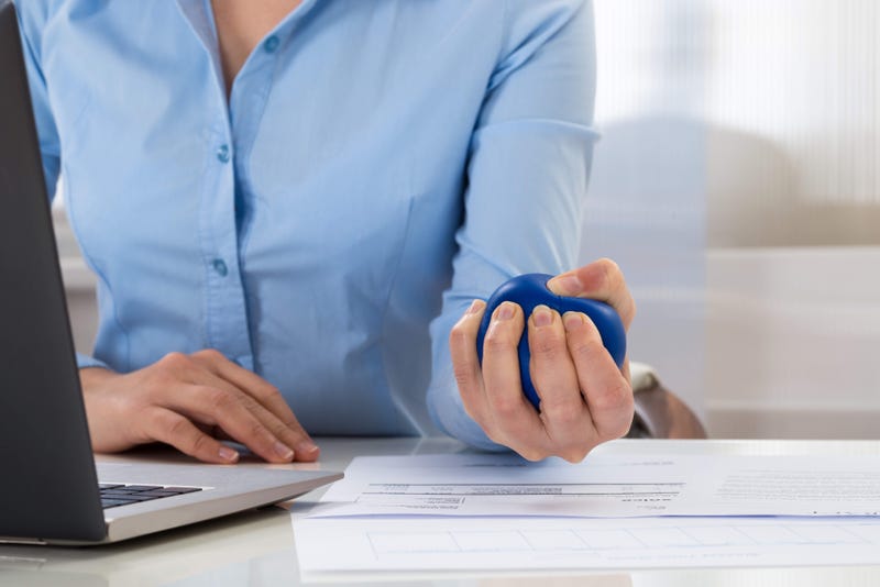 A woman squeezes a stress ball as she works on a laptop