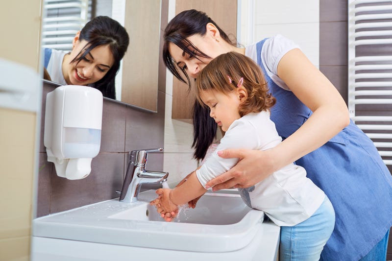 A mom helps her daughter wash her hands