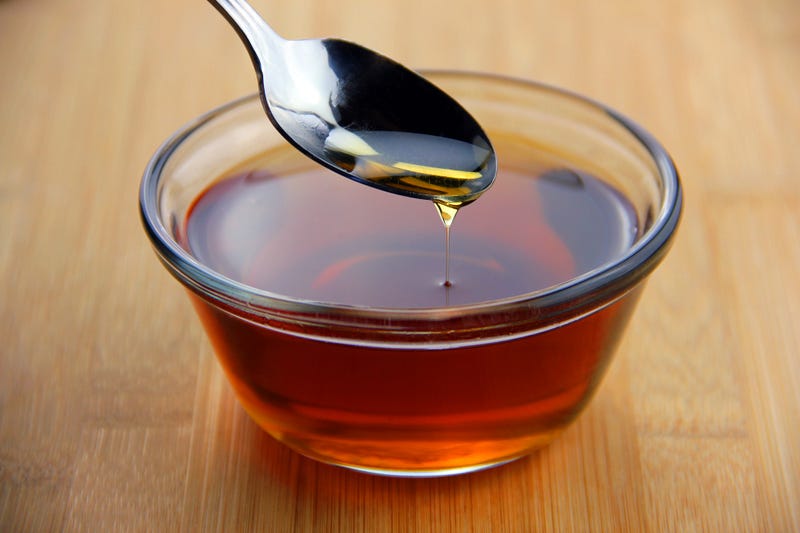 Maple syrup dripping off of a spoon into a glass bowl set on bamboo wooden surface