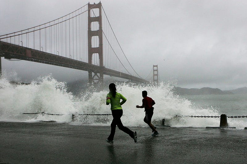 Two runners watch as a waves crash against the rocks at Fort Point near the Golden Gate Bridge December 28, 2005 in San Francisco.