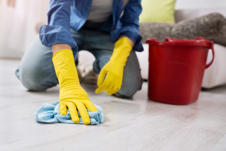 A woman cleans a floor with a water bucket and a rag