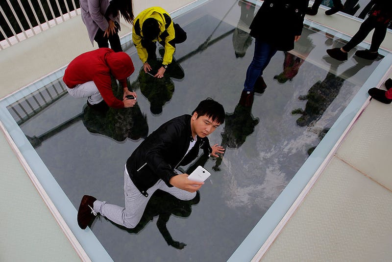 Tourists take pictures with their iphone on the glass-floor suspension bridge
