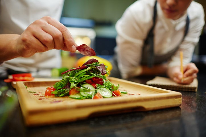 Chef putting leaf of basil on top of vegetable salad
