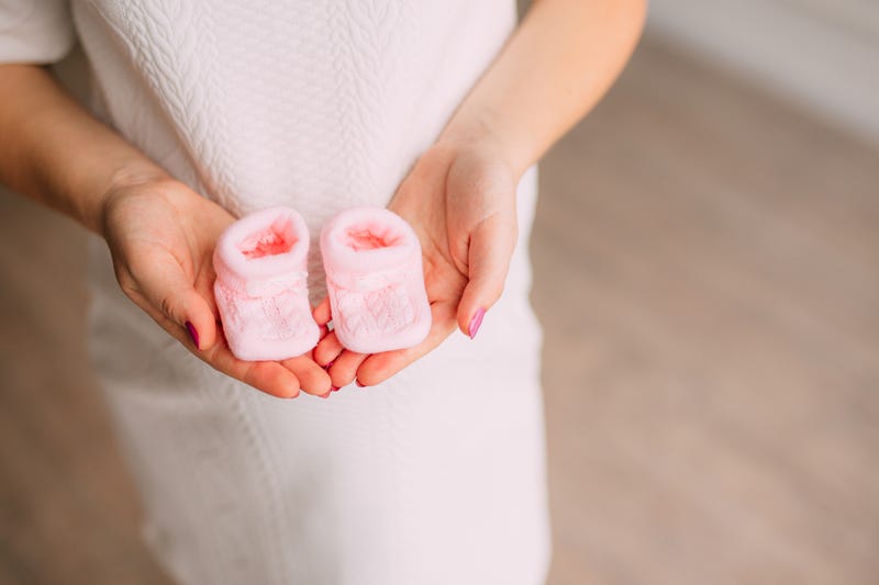 Pink baby booties in the hands of a pregnant mother.