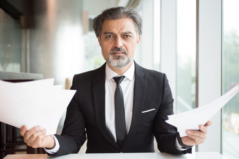 A man in a suit shrugs at documents