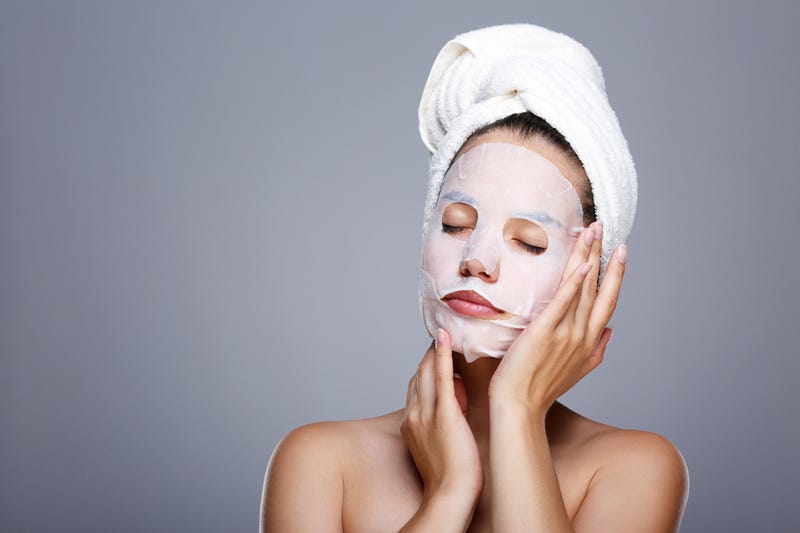 Girl with wrapped hair with towel. Closed eyes, touching skin covered by mask.