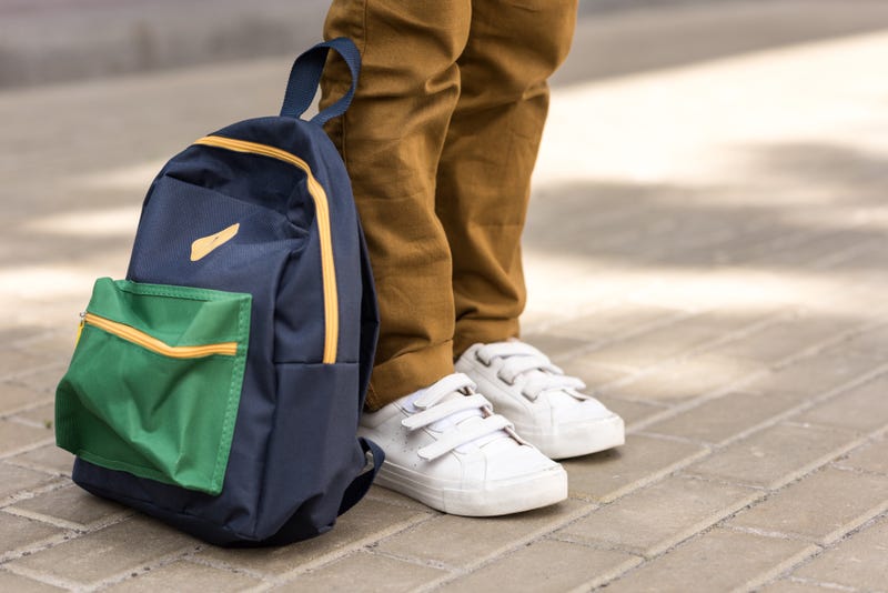student stands with backpack at his feet