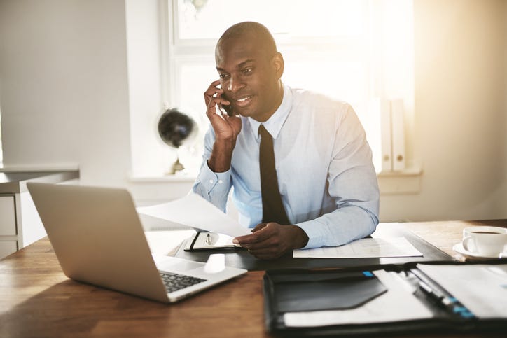 Young businessman reading paperwork over the phone and working online
