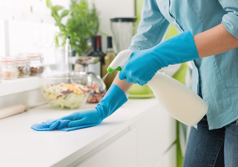 A woman in gloves sprays a kitchen counter with disinfectant
