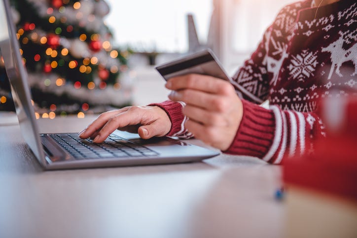 Persona hace compras en una computadora en frente de un arbol de navidad.