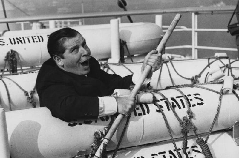 American actor and comedian Milton Berle (1908 - 2002) clowning about with a broom on the deck of the 'SS United States' during an east-west crossing of the Atlantic, 15th July 1952