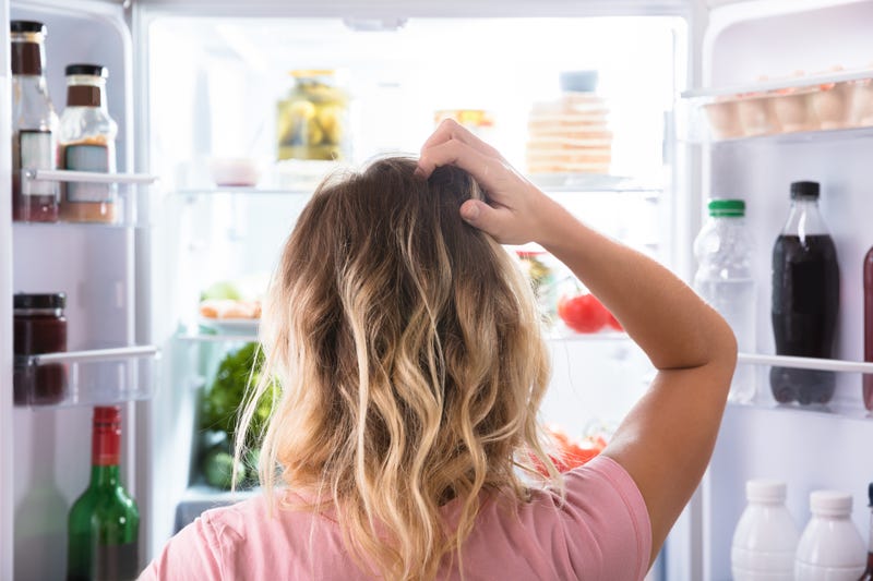 A confused woman stands in front of an open refrigerator