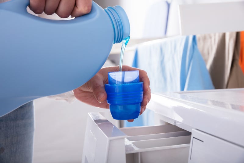 A person pouring detergent into a cap before loading into a washer