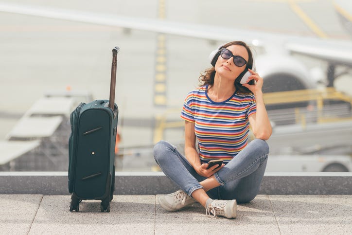 girl with headphones on next to a suitcase