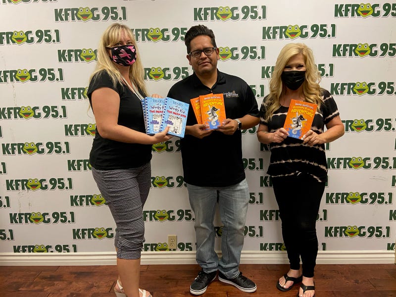 K-Frog's Pepper and Heather Froglear present Joe Ramos of the Miracles and Dreams Foundation with books for their holiday toy drive