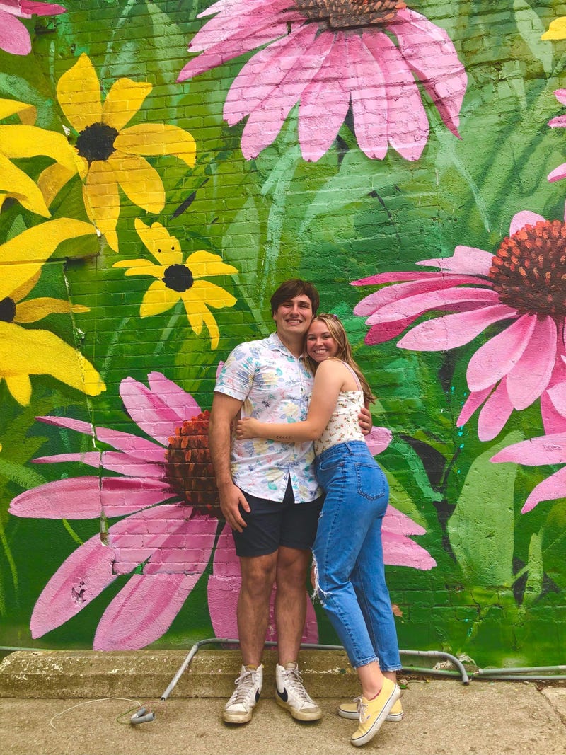 A man and woman hugging each other in front of flower mural