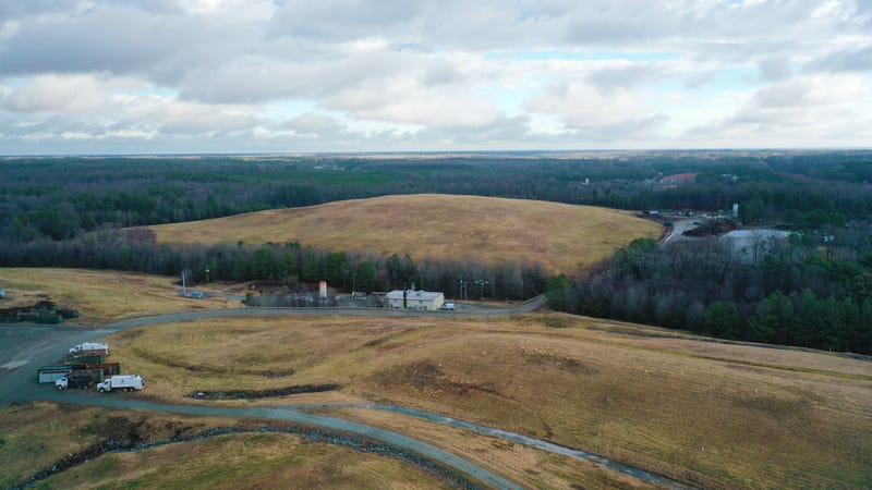 Grassy hills rise above a forest. A gravel road winds between them.