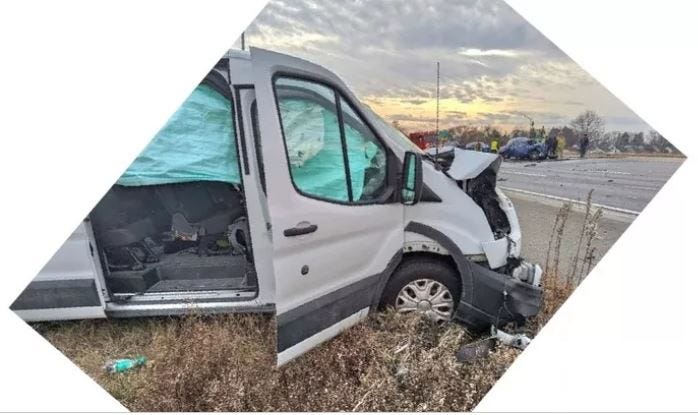 The Goodell family van -- a white Ford Transit -- sits on the side of the highway. It is damaged from a crash. The hood is bent up, front bumper falling off, headlights smashed. All airbags are deployed and are hanging in the windows.