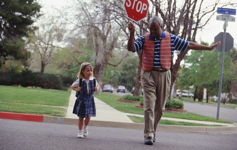 A crossing guard helps a young girl cross the street