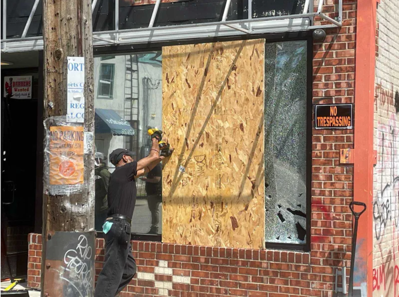 A worker boards up a storefront after it was hit with gunfire on Tuesday morning