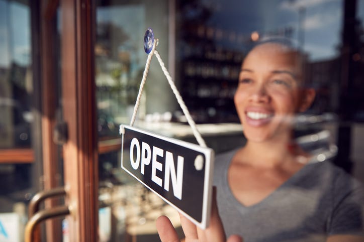 Black woman turns sign to "Open" at front of small business