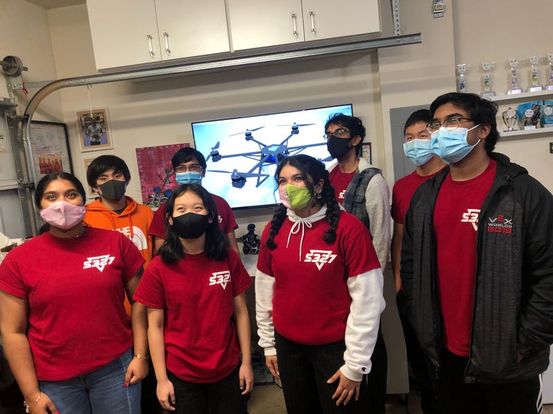 Students pose in front of a rendering of the drone.