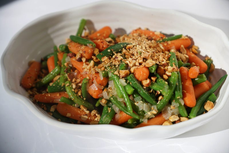 A serving dish filled with green beans, carrots, and chopped nuts