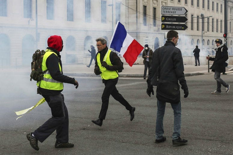 A demonstrator carries a French flag as yellow vest demonstrators are hit by tear gas during clashes in Lyon, central France, Saturday, Jan. 26, 2019.