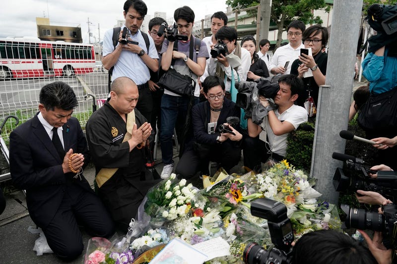 Japanese Diet member, Kenta Izumi, left, and Buddhist monk, Matsumoto Genkun, pay respects at a makeshift memorial site in front of burned Kyoto Animation Studio building, background left, Friday, July 19, 2019, in Kyoto, Japan.