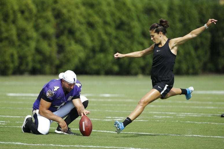 Baltimore Ravens' Sam Koch holds the ball for United States soccer player Carli Lloyd as she attempts to kick a field goal after the Philadelphia Eagles and the Baltimore Ravens held a joint NFL football practice in Philadelphia, Tuesday, Aug. 20, 2019.