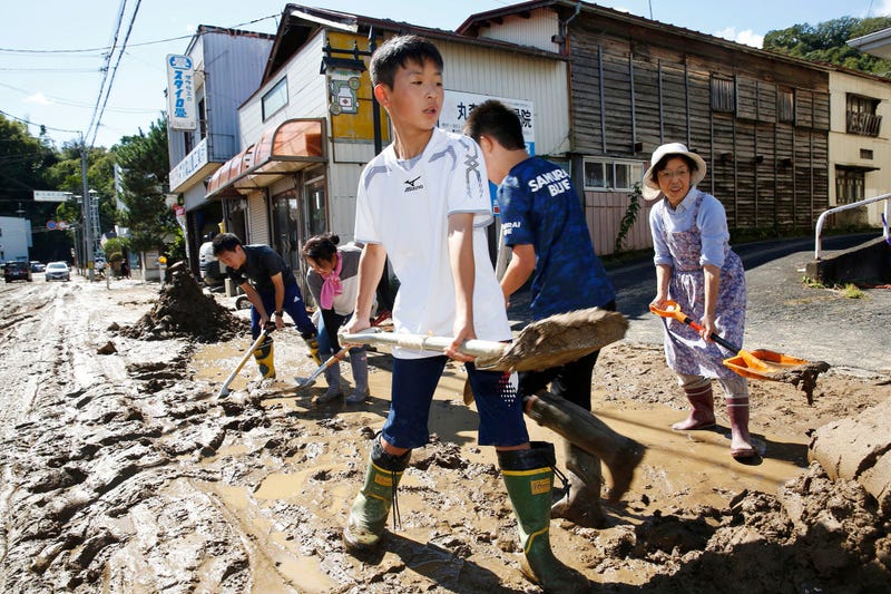 Students and residents scoop dirt as the town is flooded Typhoon Hagibis, in Marumori, Miyagi prefecture, northern Japan, Sunday, Oct. 13, 2019.