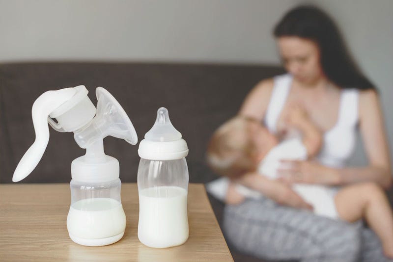 Bottle and breast pump with breast milk on the background of mother holding in her hands and breastfeeding baby