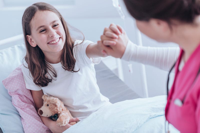 Nurse holding smiling girls hand in hospital bed